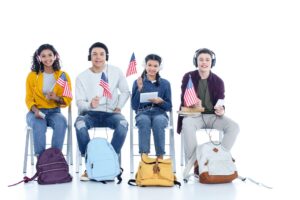 group of teen students in headphones with usa flags sitting on chairs isolated on white
