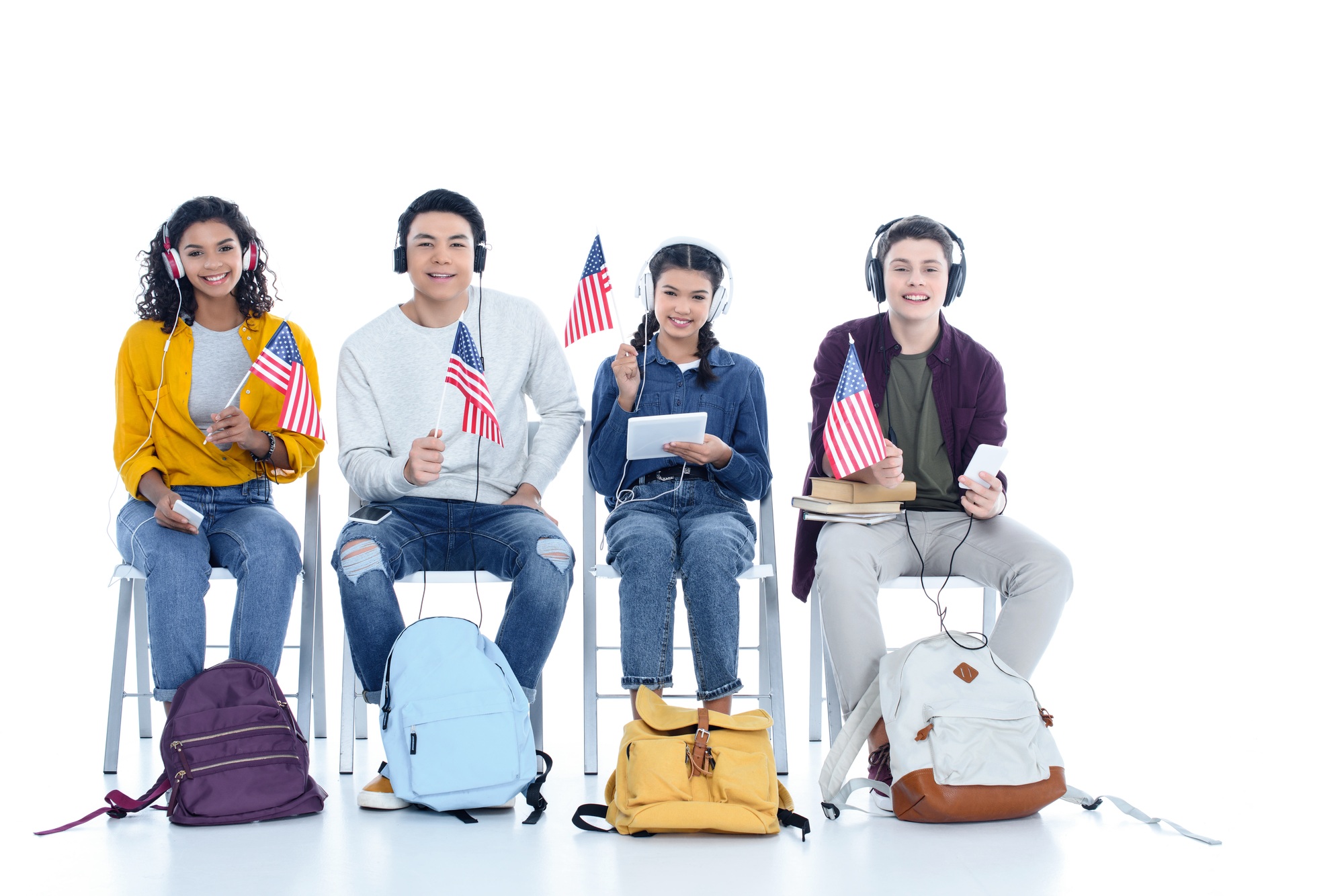 group of teen students in headphones with usa flags sitting on chairs isolated on white